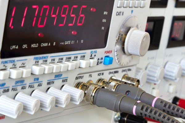 A close-up of a laboratory function generator with a frequency counter.