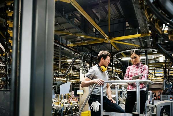 Two industry professionals discuss engineering notes in a manufacturing facility. 